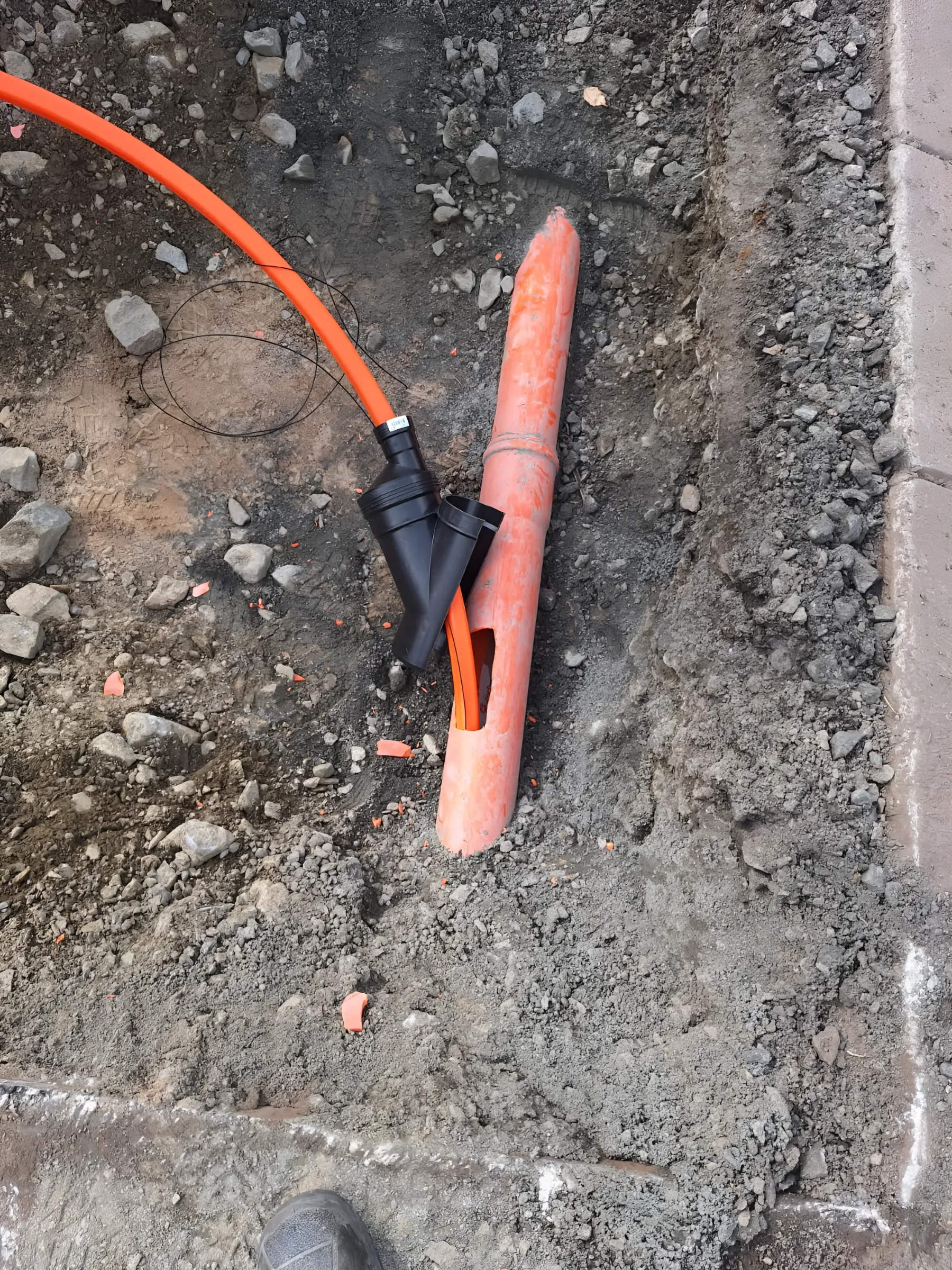 Orange dräneringsrör med grenrör i en öppen schakt