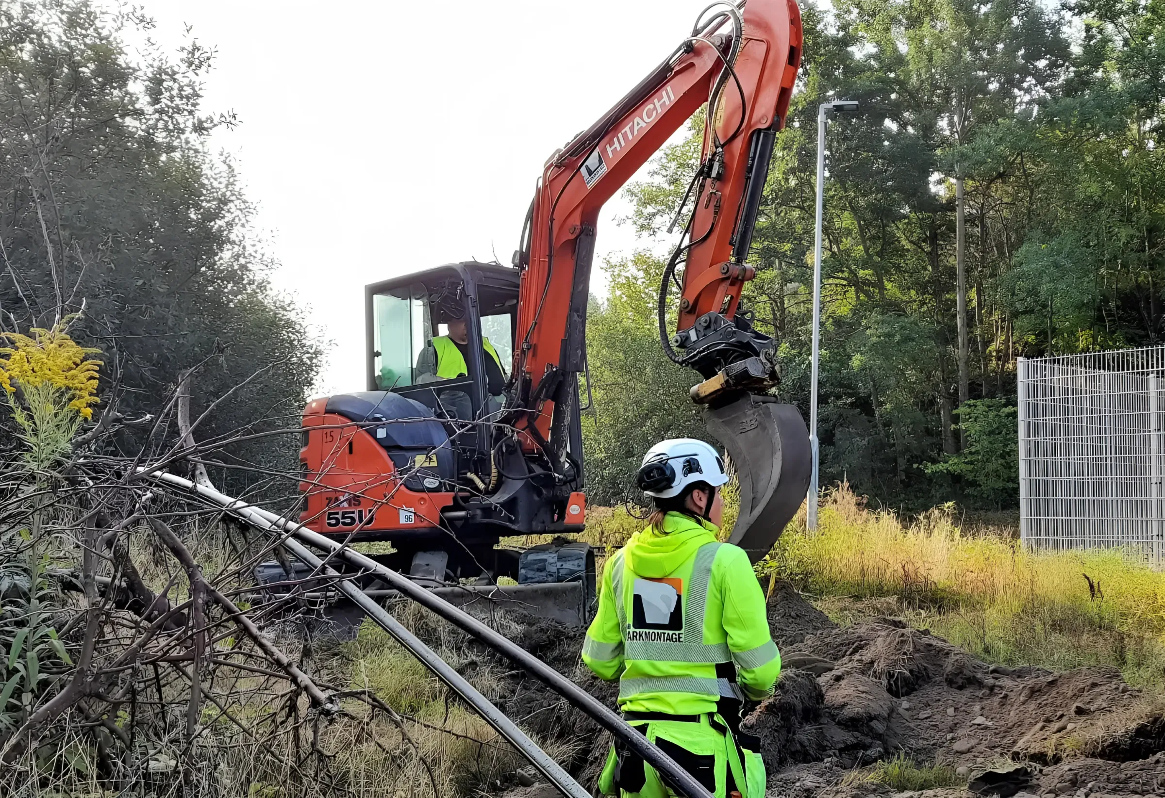 Grävmaskin och medarbetare i varselkläder vid en schakt
